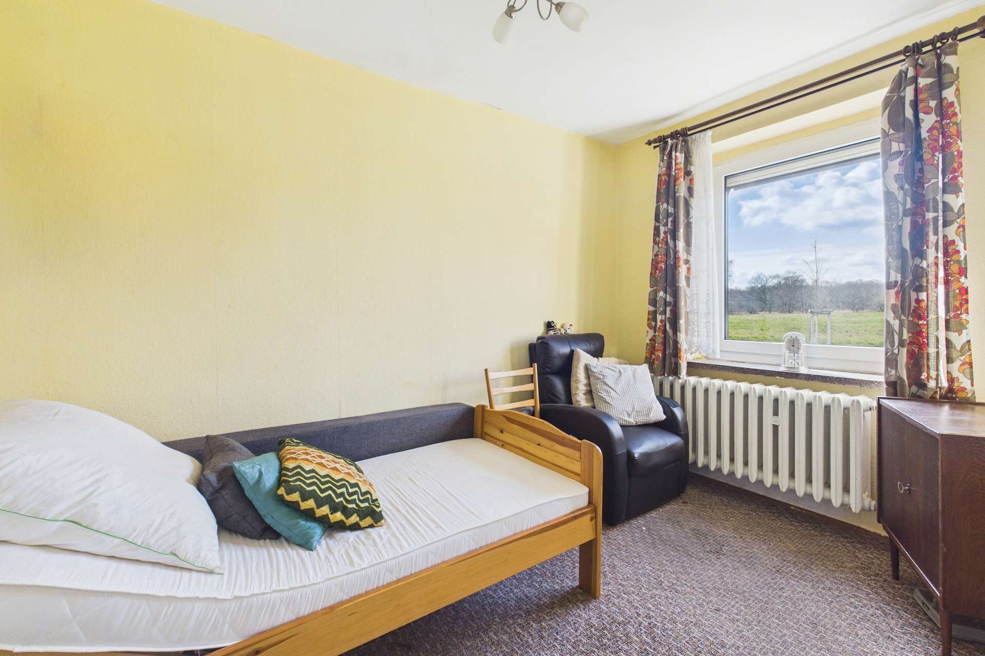 Ein einfaches Schlafzimmer mit einem Einzelbett, einem Sessel, einem Fenster und gelben Wänden.