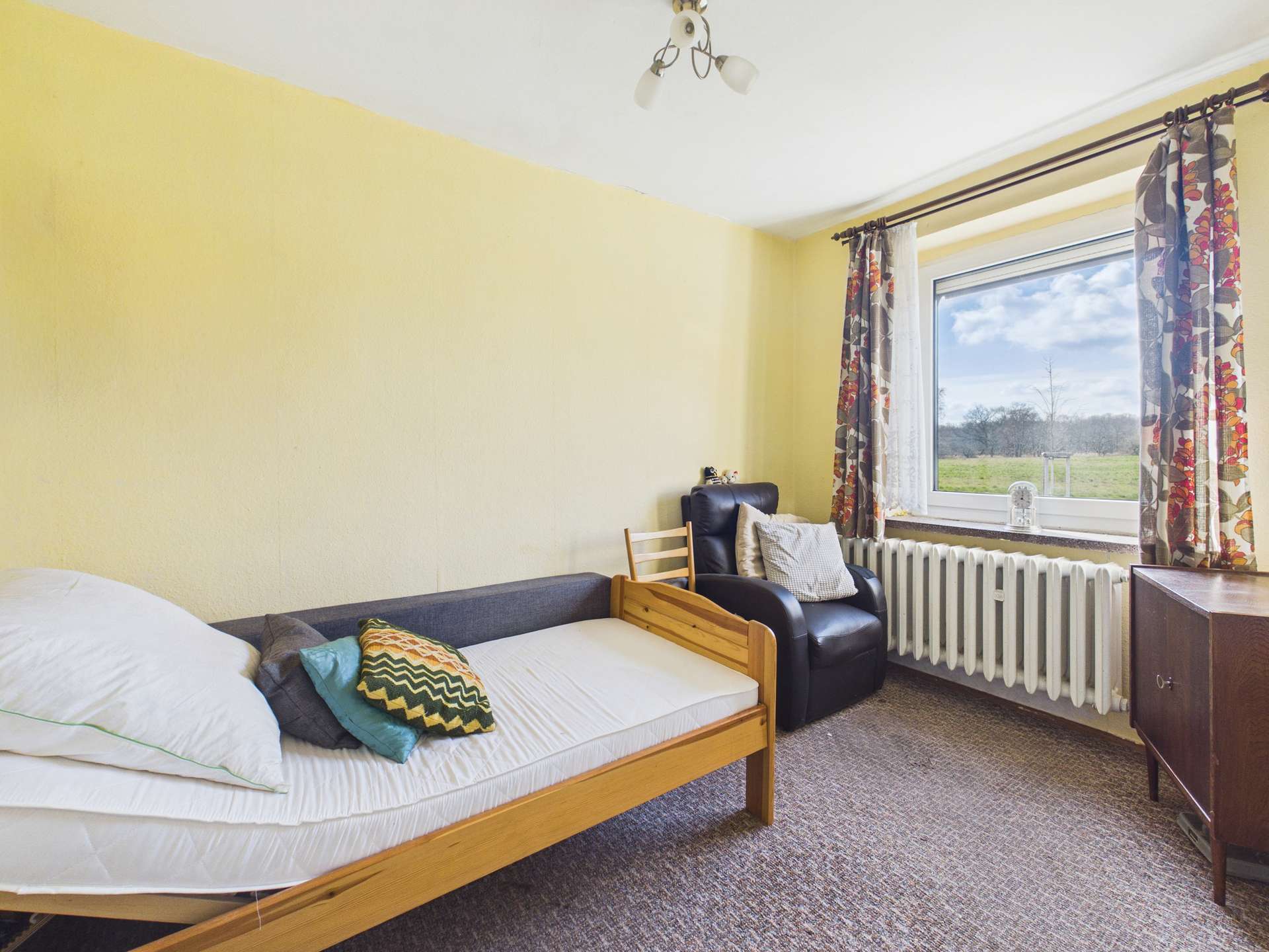 Ein einfaches Schlafzimmer mit einem Einzelbett, einem Sessel, einem Fenster und gelben Wänden.