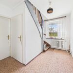 Heller Flur mit Treppe, Fenster und Heizkörper; beige Teppichboden und weiße Wände schaffen eine freundliche Atmosphäre.