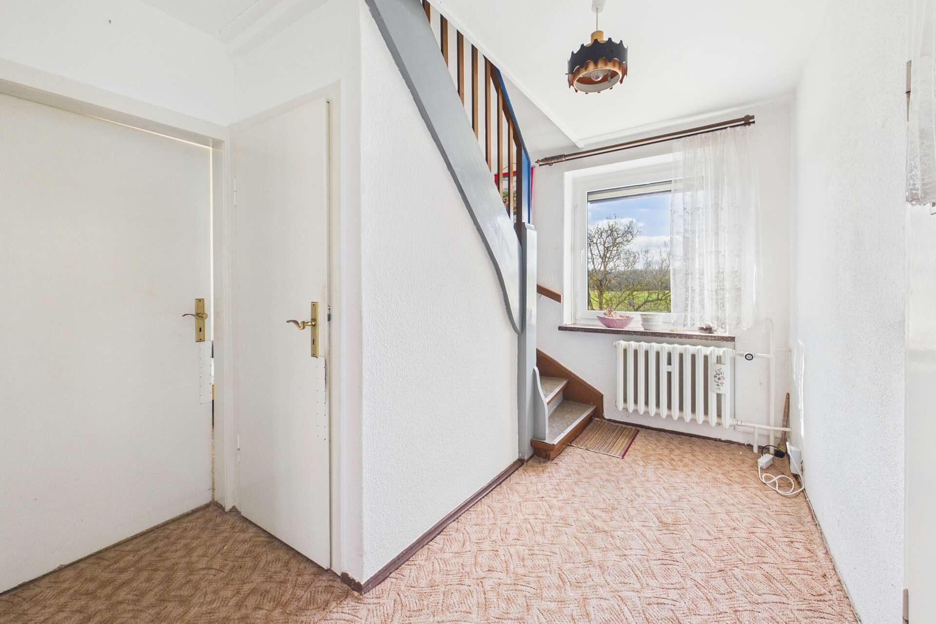 Heller Flur mit Treppe, Fenster und Heizkörper; beige Teppichboden und weiße Wände schaffen eine freundliche Atmosphäre.