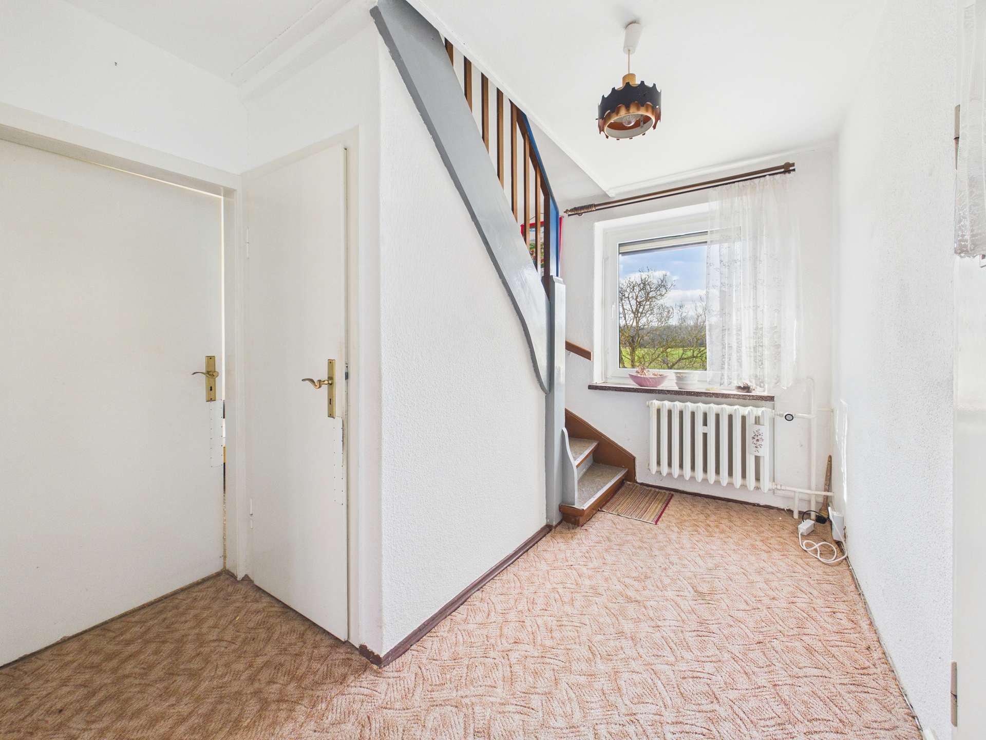 Heller Flur mit Treppe, Fenster und Heizkörper; beige Teppichboden und weiße Wände schaffen eine freundliche Atmosphäre.