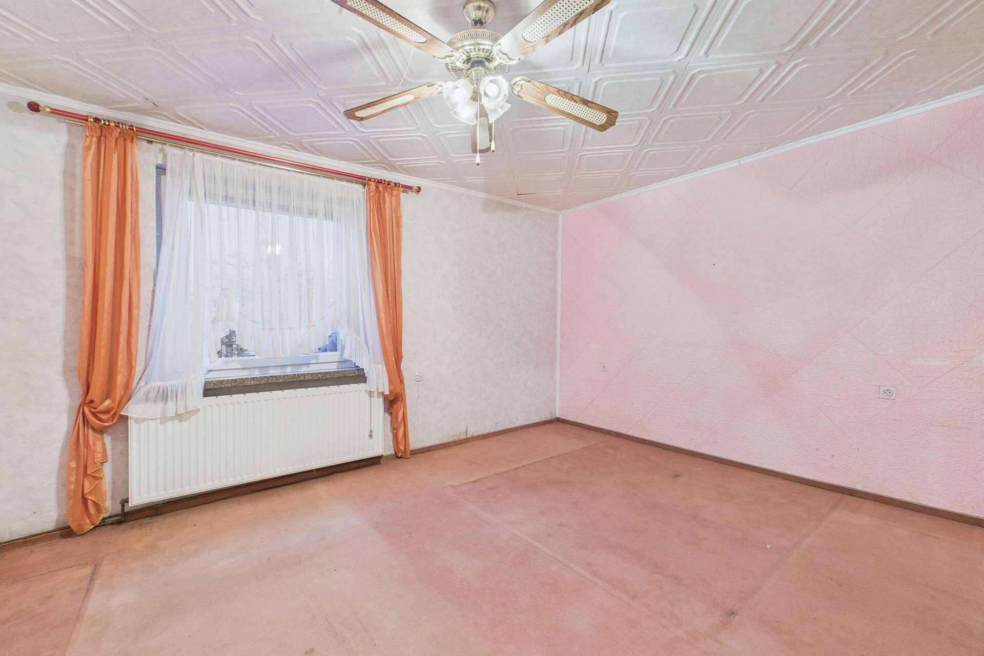 Leerer Raum mit pinken Wänden, einem Fenster mit Vorhängen und einem Deckenventilator.
