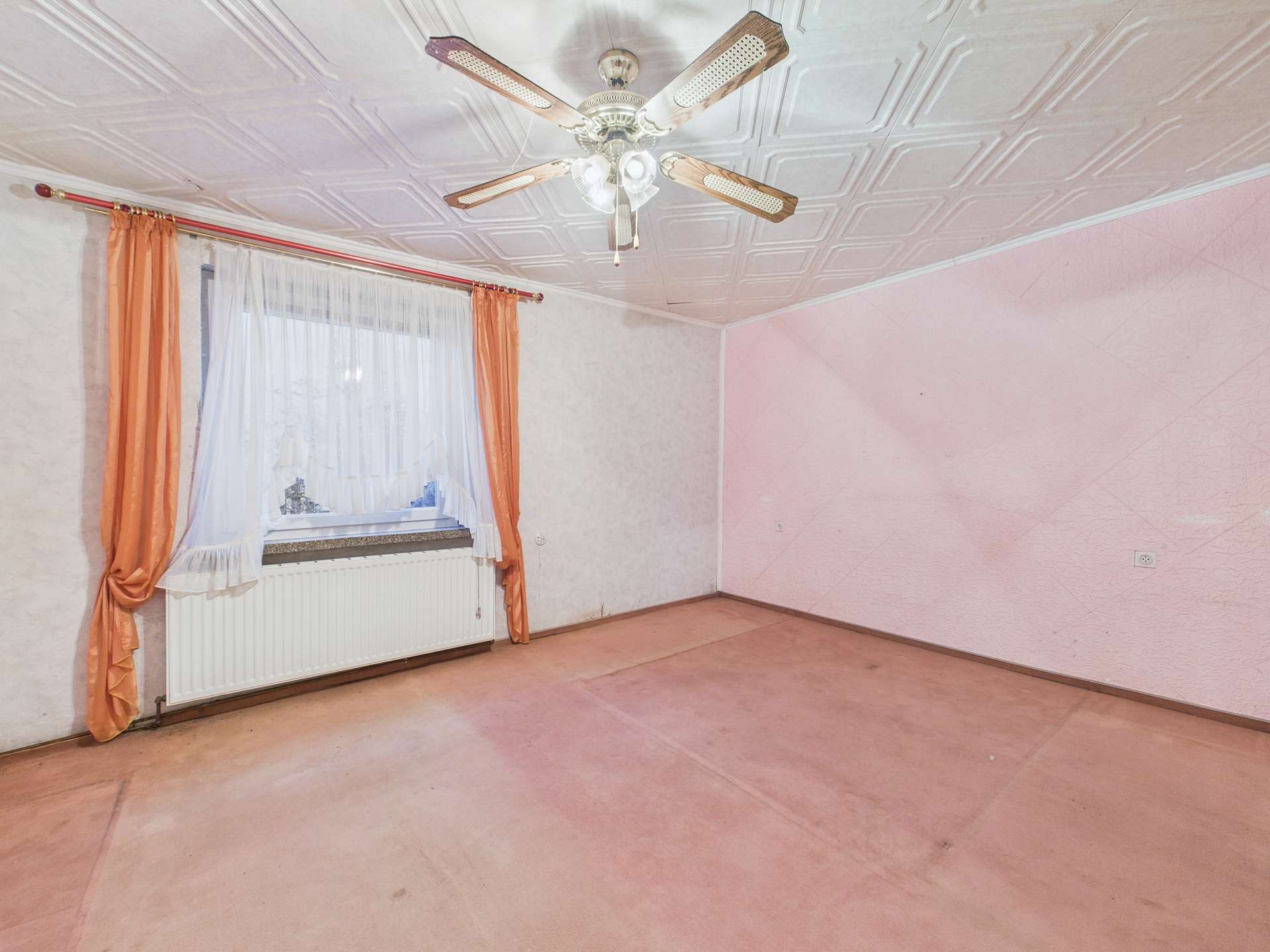Leerer Raum mit pinken Wänden, einem Fenster mit Vorhängen und einem Deckenventilator.