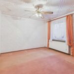 Leerer Raum mit Teppichboden, Deckenventilator und Fenster mit Vorhängen. Wände in hellem Muster.