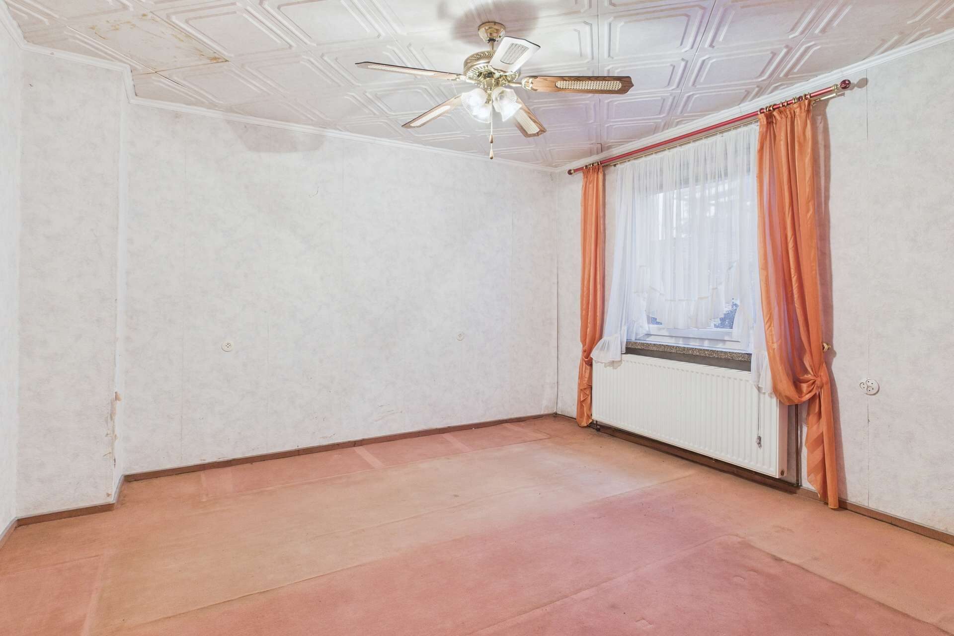 Leerer Raum mit Teppichboden, Deckenventilator und Fenster mit Vorhängen. Wände in hellem Muster.