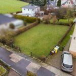 Luftaufnahme eines gepflegten Gartens mit Rasen, umgeben von Hecken und einem Parkplatz neben einem Wohnhaus.
