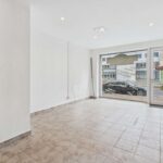 Leere Ladenfläche mit hellen Wänden, gefliestem Boden und großen Fenstern zur Straßenseite.