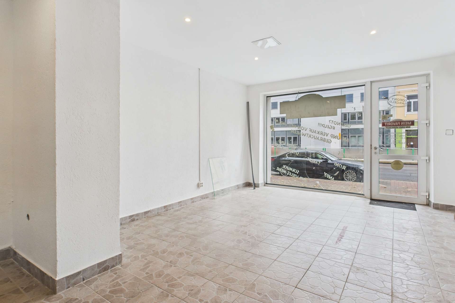 Leere Ladenfläche mit hellen Wänden, gefliestem Boden und großen Fenstern zur Straßenseite.