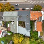 Luftaufnahme eines Wohngebiets mit verschiedenen Dachformen und Bäumen, umgeben von Straßen und parkenden Autos.