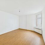 Leerer Raum mit hellem Holzfußboden, weißen Wänden und einem Fenster, das natürliches Licht hereinlässt.