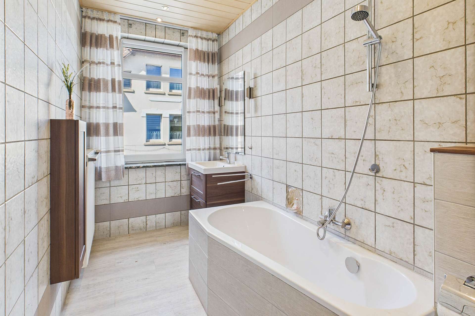 Helles Badezimmer mit Badewanne, Dusche und Holzregalen, gefliest mit neutralen Farben und Fensterblick.