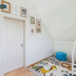 Ein helles Kinderzimmer mit einem Bett, einem Teppich mit Tieren und gerahmten Bildern an der Wand.
