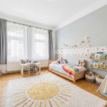 Helles Kinderzimmer mit einem bunten Bett, Spielzeug, einem Teppich in Sonnenform und einem Spielzelt.