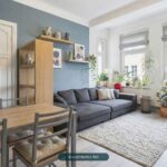 Heller Wohnraum mit grauem Sofa, Esstisch und Pflanzen, dekoriert mit modernen Kunstwerken und Vasen.