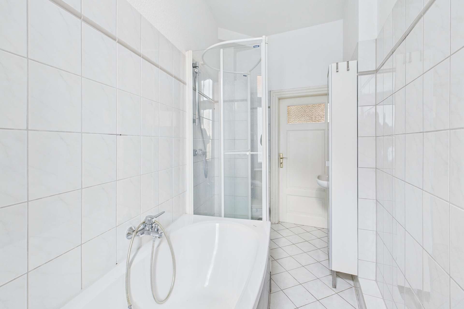 Badezimmer mit Dusche, Badewanne und weißen Fliesen, helle und moderne Gestaltung.