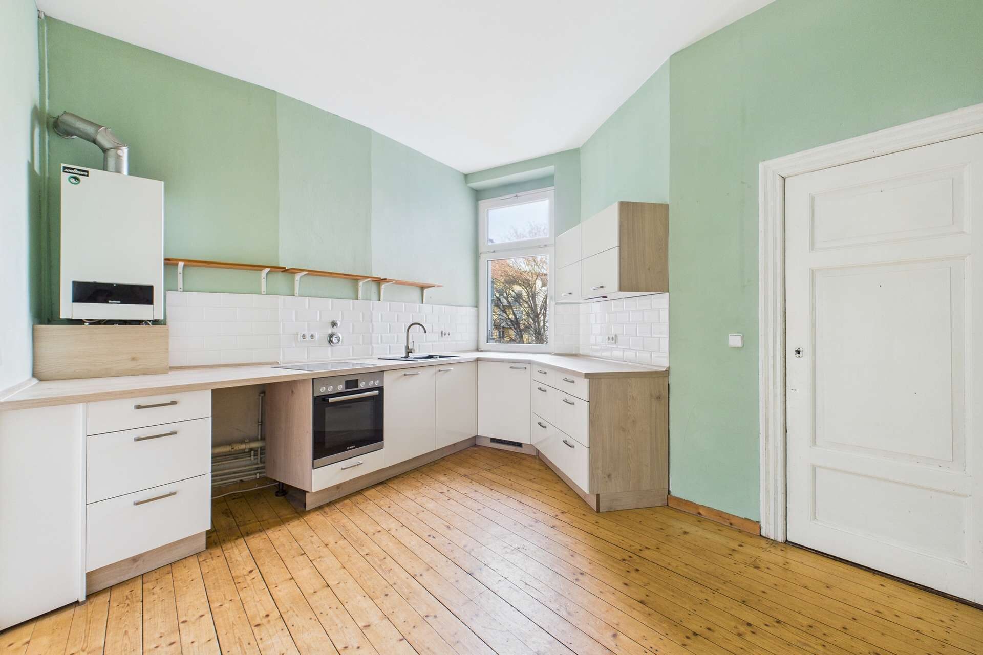 Moderne Küche mit hellgrünen Wänden, Holzfußboden und weißen Küchenschränken sowie einem Fenster zur natürlichen Beleuchtung.