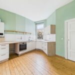 Moderne Küche mit hellgrünen Wänden, Holzfußboden, Fenster und integrierten Geräten.