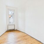 Leerer Raum mit Holzboden und Fenster, Wände in neutralem Weiß, minimalistische Gestaltung.