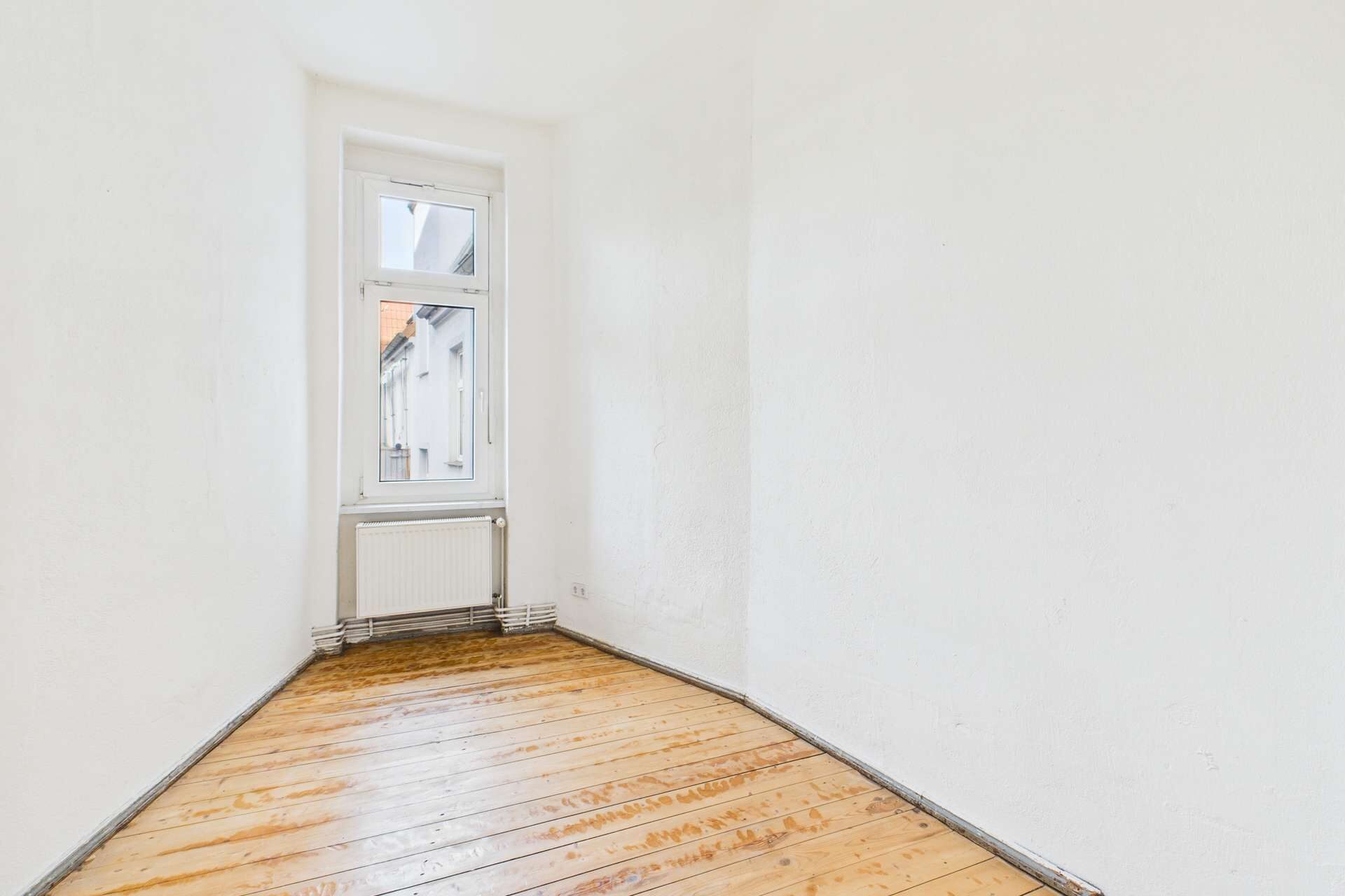 Leerer Raum mit Holzboden und Fenster, Wände in neutralem Weiß, minimalistische Gestaltung.