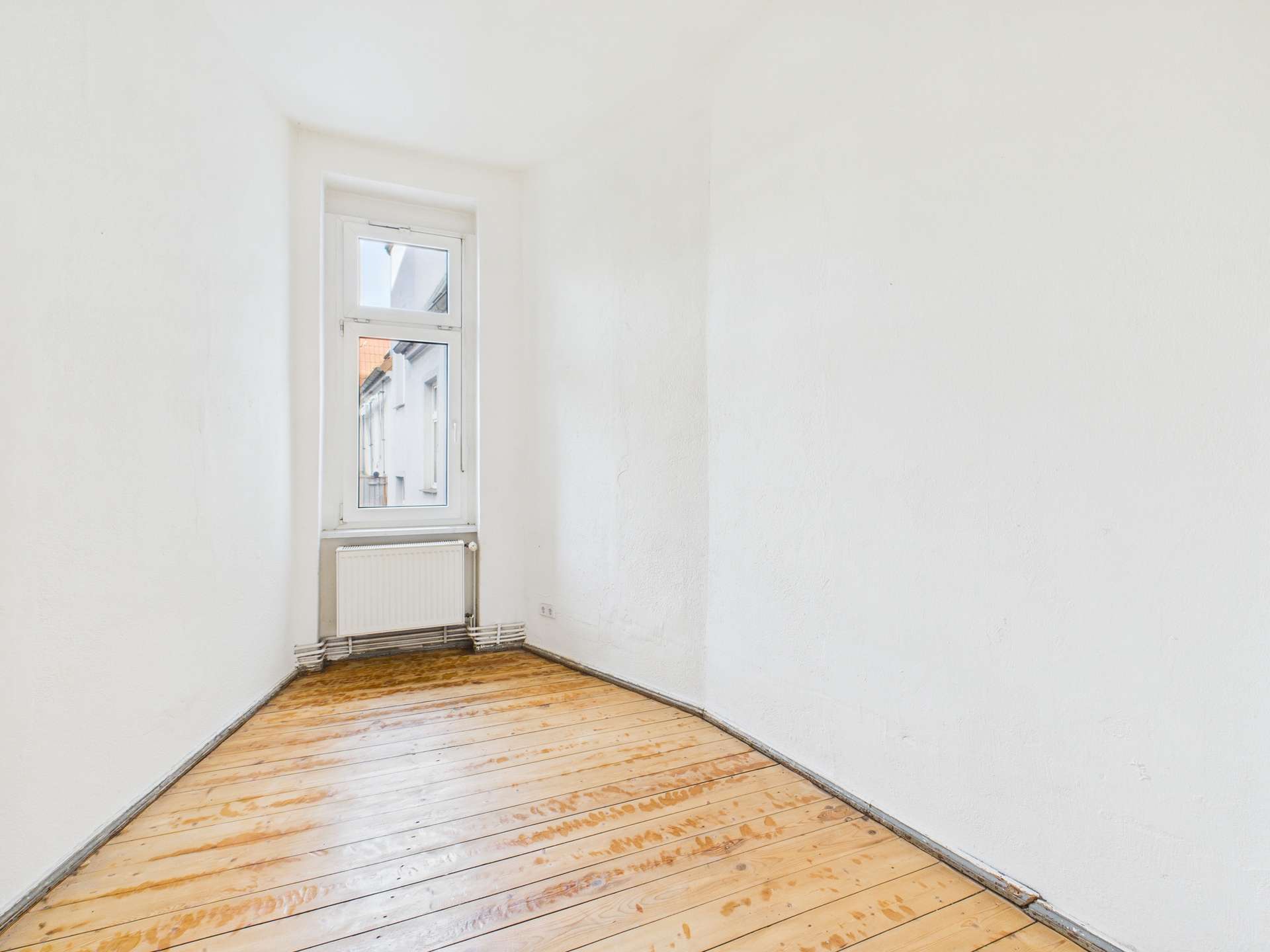 Leerer Raum mit Holzboden und Fenster, Wände in neutralem Weiß, minimalistische Gestaltung.