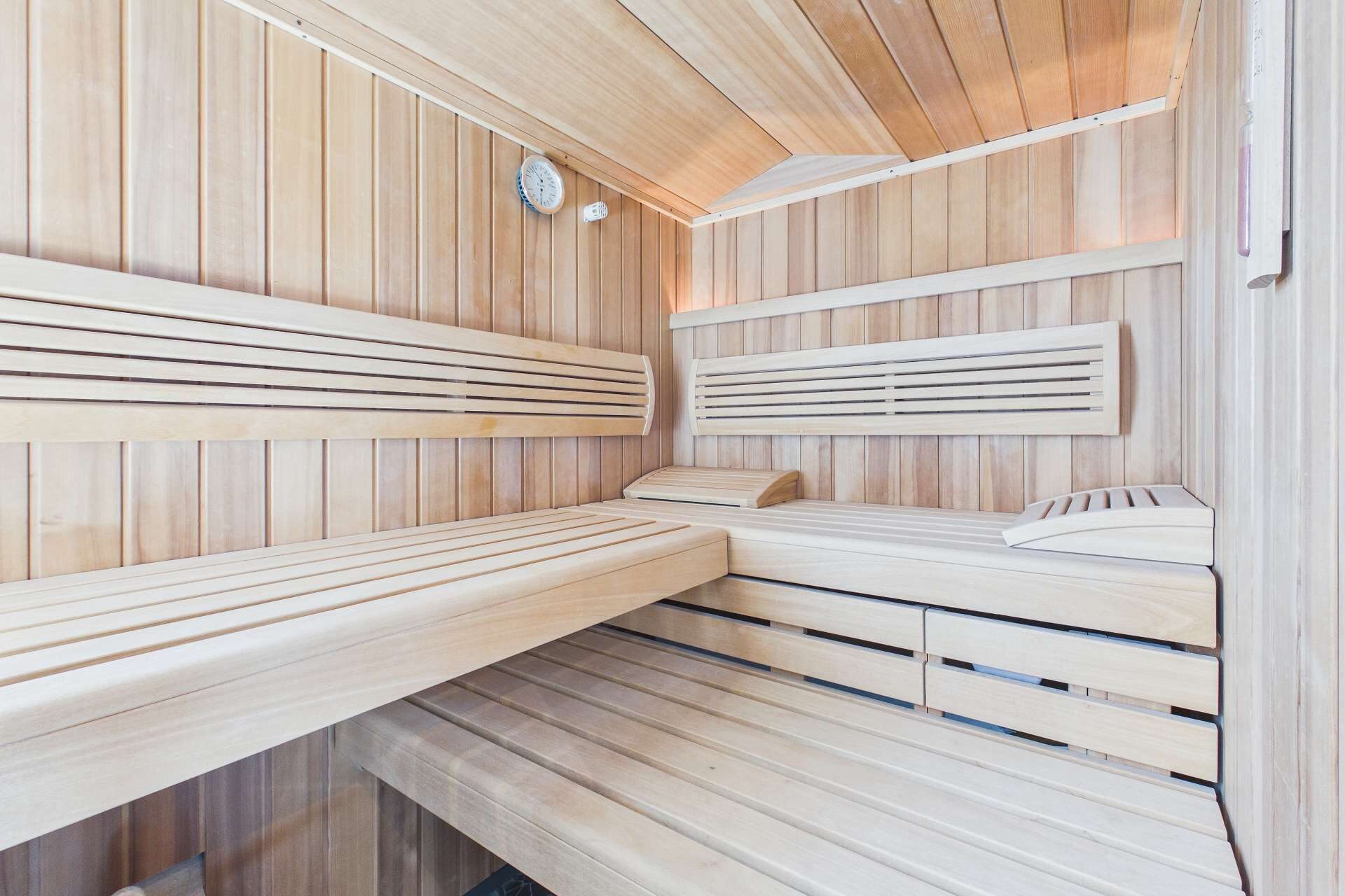 Innenansicht einer Holzsauna mit Bänken, Holzverkleidung und einer Wanduhr.
