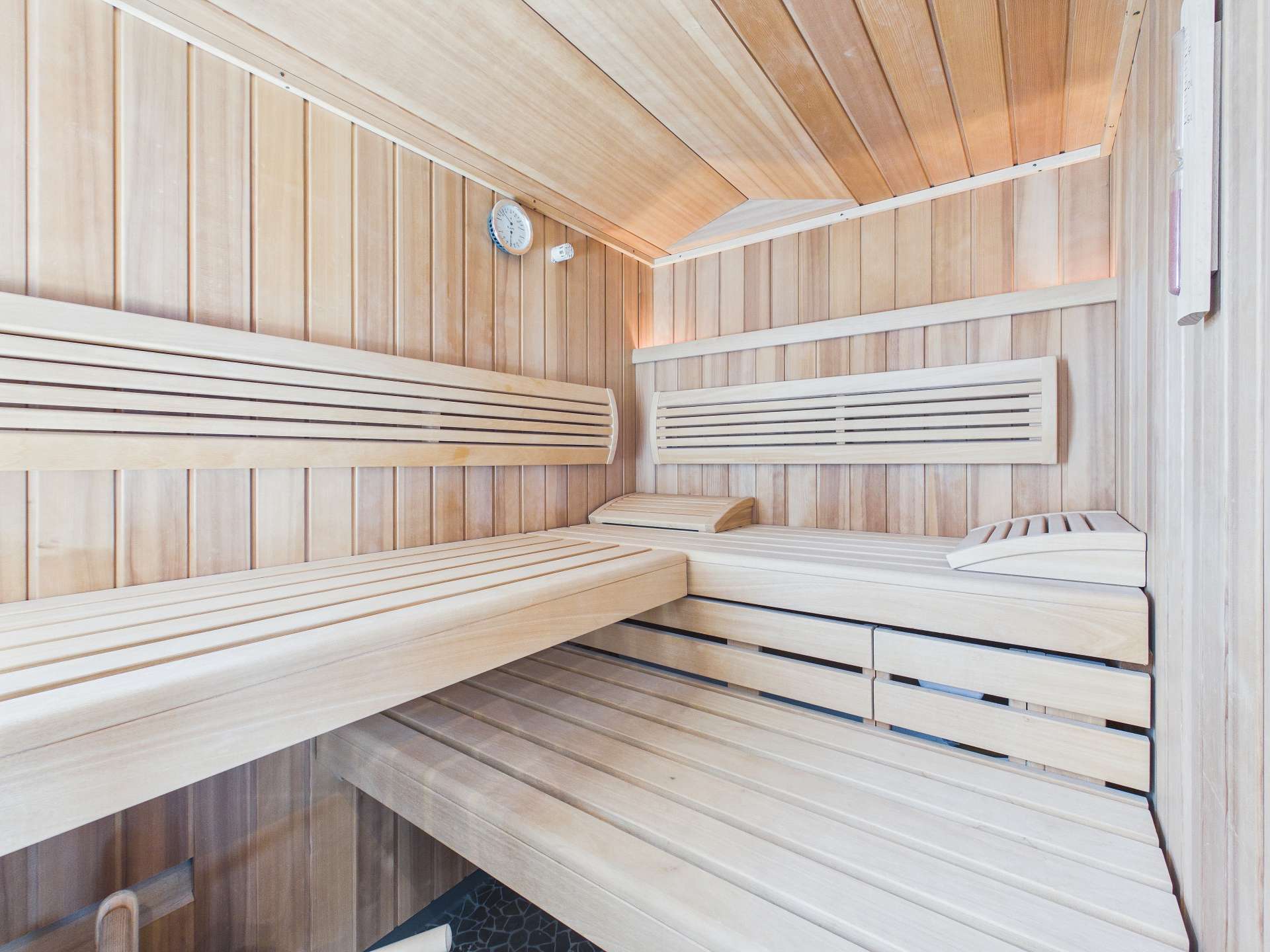Innenansicht einer Holzsauna mit Bänken, Holzverkleidung und einer Wanduhr.