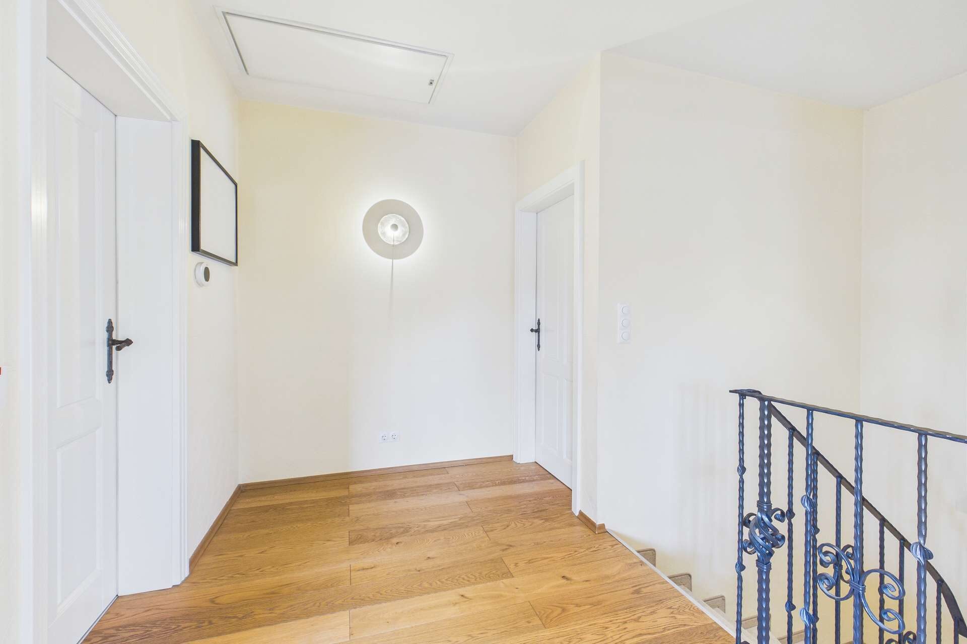 Heller Flur mit Holzfußboden, Wandleuchte und Treppe, umgeben von weißen Wänden und Türen.