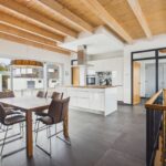 Moderne Küche mit Holzbalkendecke, Esstisch und eleganten Stühlen in einem lichtdurchfluteten Raum.