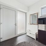 Heller Eingangsbereich mit weißer Tür, Spiegel, Sitzbank und schwarzem Regal mit Aufbewahrungsboxen.