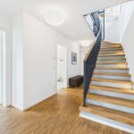 Heller Flur mit Holztreppe, minimalistischer Gestaltung und Zugang zu mehreren Räumen.