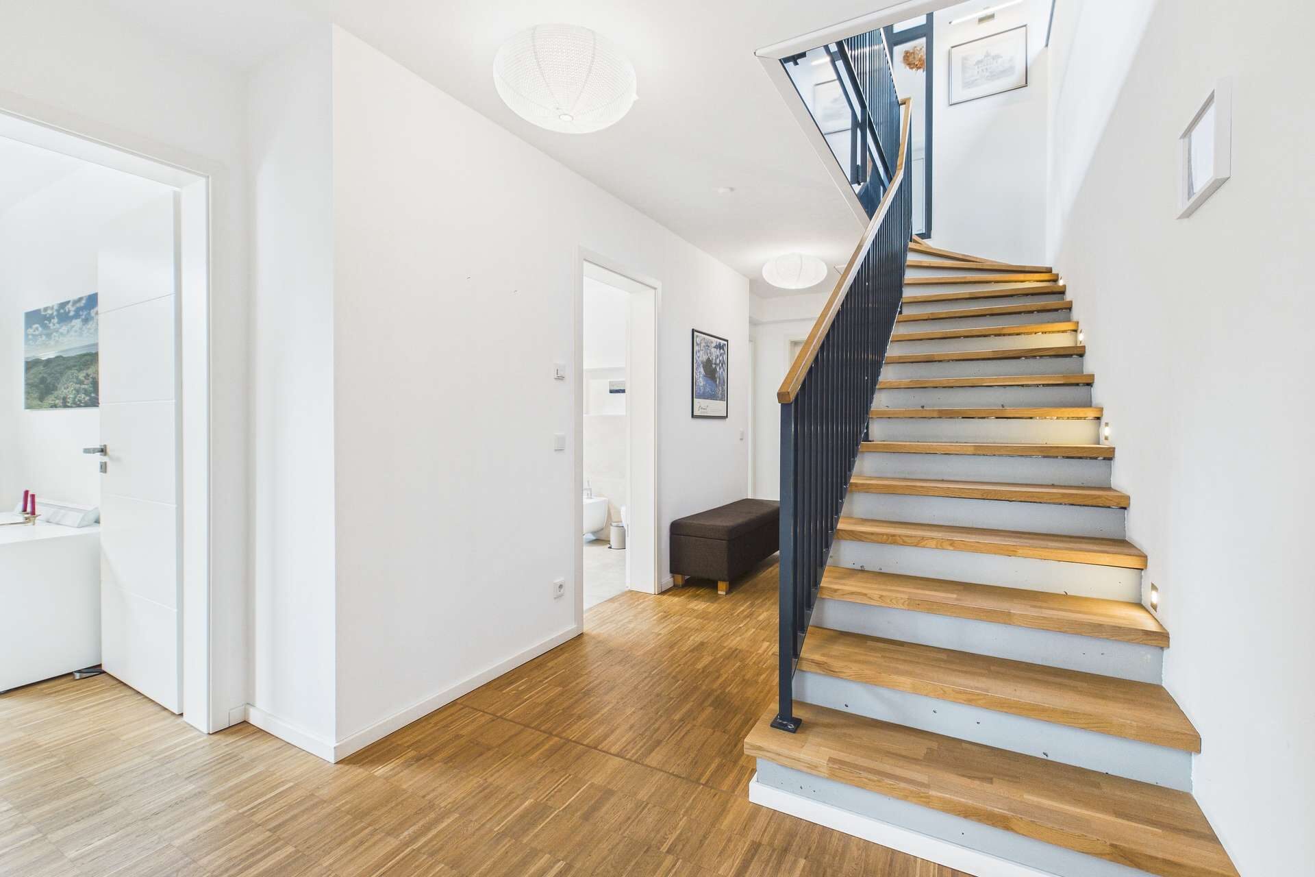 Heller Flur mit Holztreppe, minimalistischer Gestaltung und Zugang zu mehreren Räumen.