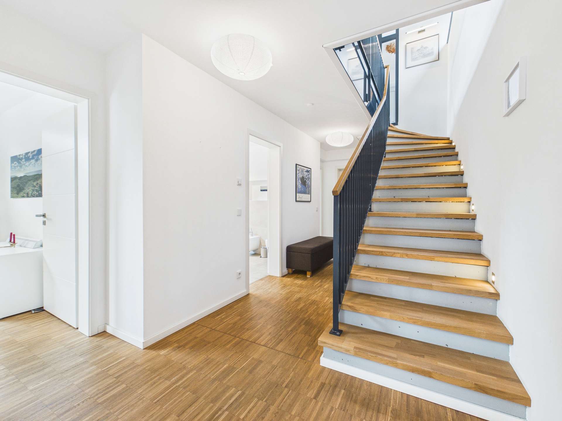 Heller Flur mit Holztreppe, minimalistischer Gestaltung und Zugang zu mehreren Räumen.