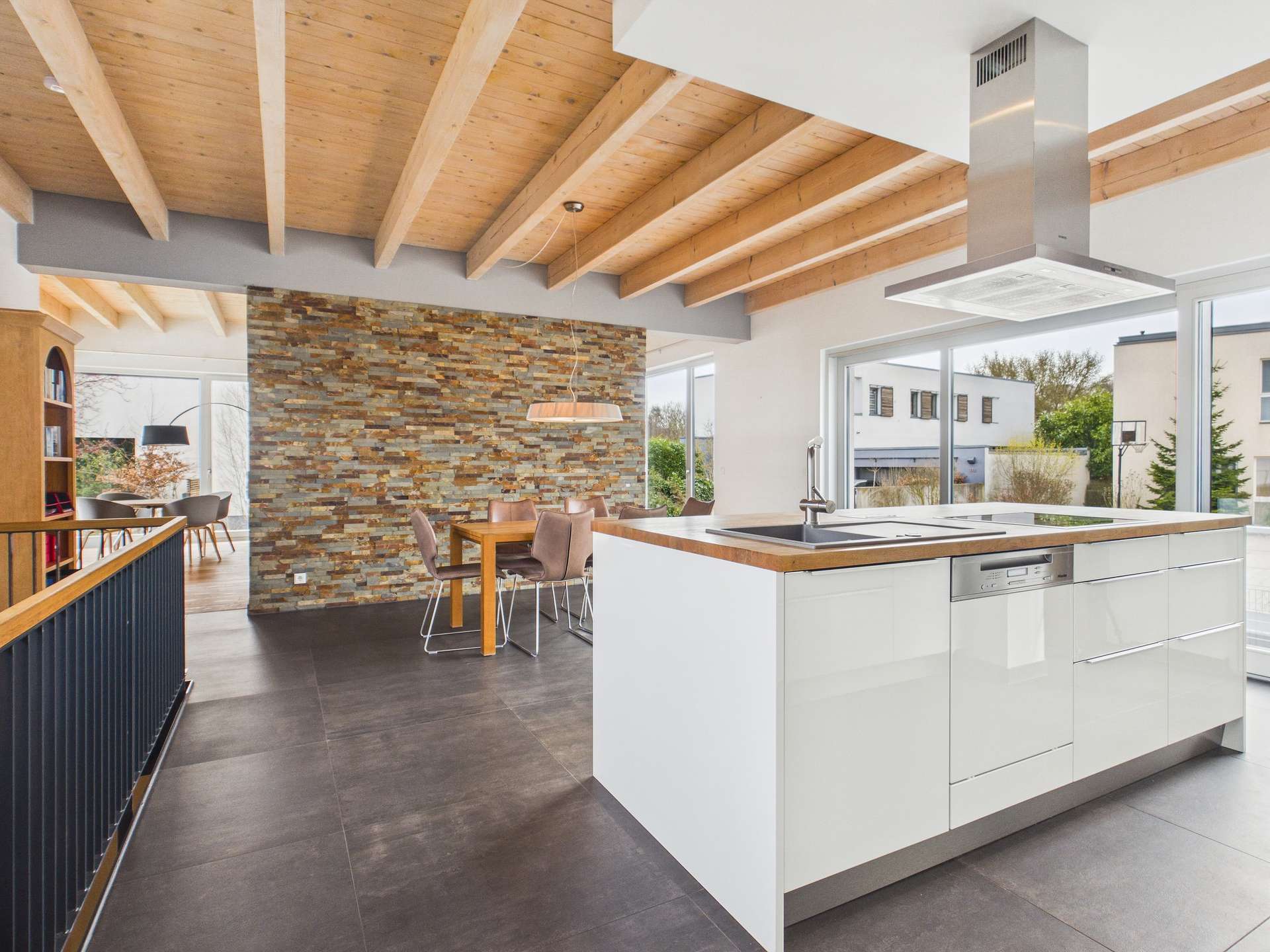 Moderne Küche mit Holzdecken, Steinwand und Essbereich, große Fenster für viel Tageslicht.