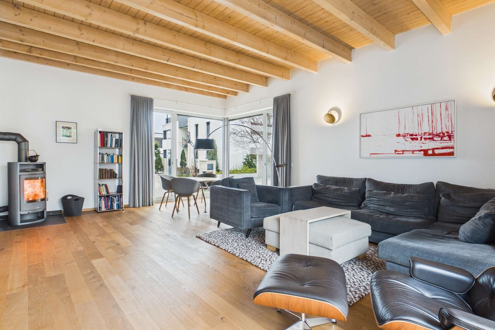 Modernes Wohnzimmer mit Holzdecke, gemütlichem Sofa, Kamin und großem Fenster, das auf eine Landschaft blickt.