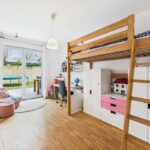 Kinderzimmer mit Hochbett, Schreibtisch, Stauraum und Zugang zu einem Garten durch große Fenster.