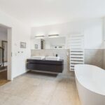Modernes Badezimmer mit freistehender Badewanne, Doppelwaschbecken und Holztreppe im Hintergrund.