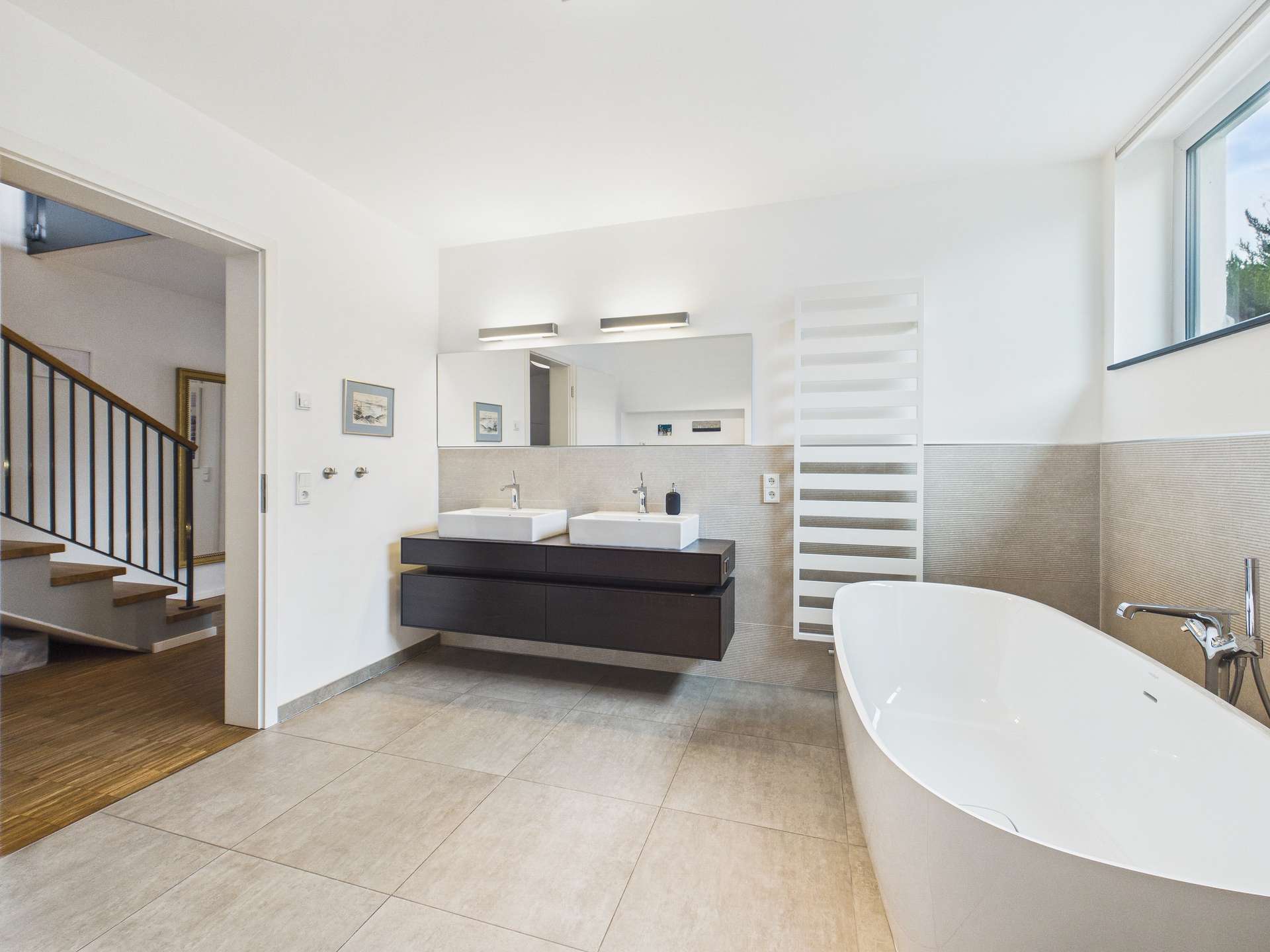 Modernes Badezimmer mit freistehender Badewanne, Doppelwaschbecken und Holztreppe im Hintergrund.