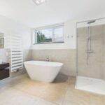 Modernes Badezimmer mit freistehender Badewanne, Dusche, großem Fenster und eleganten Fliesen.