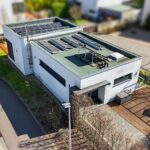 Modernes Einfamilienhaus mit Solaranlage, umgeben von Grünflächen und Gehweg, in einer ruhigen Wohngegend.