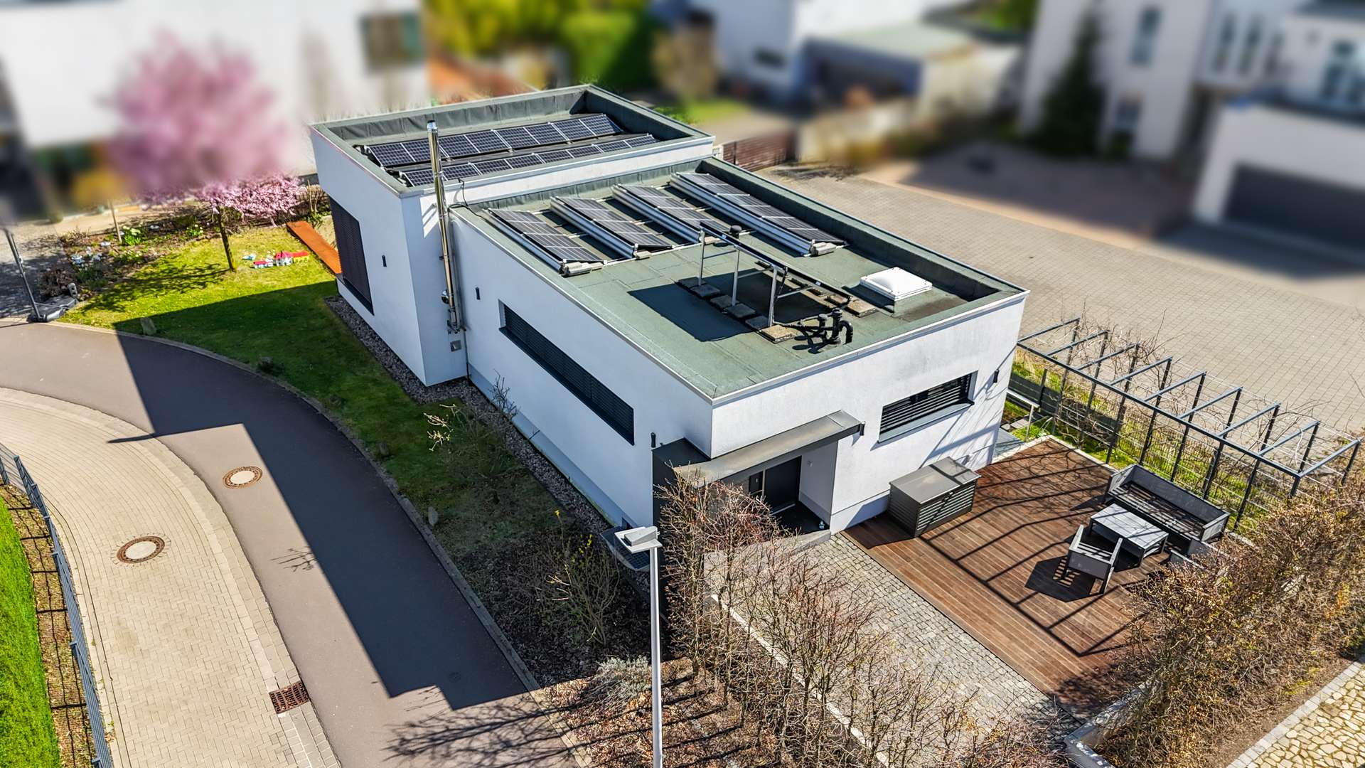 Modernes Einfamilienhaus mit Solaranlage, umgeben von Grünflächen und Gehweg, in einer ruhigen Wohngegend.