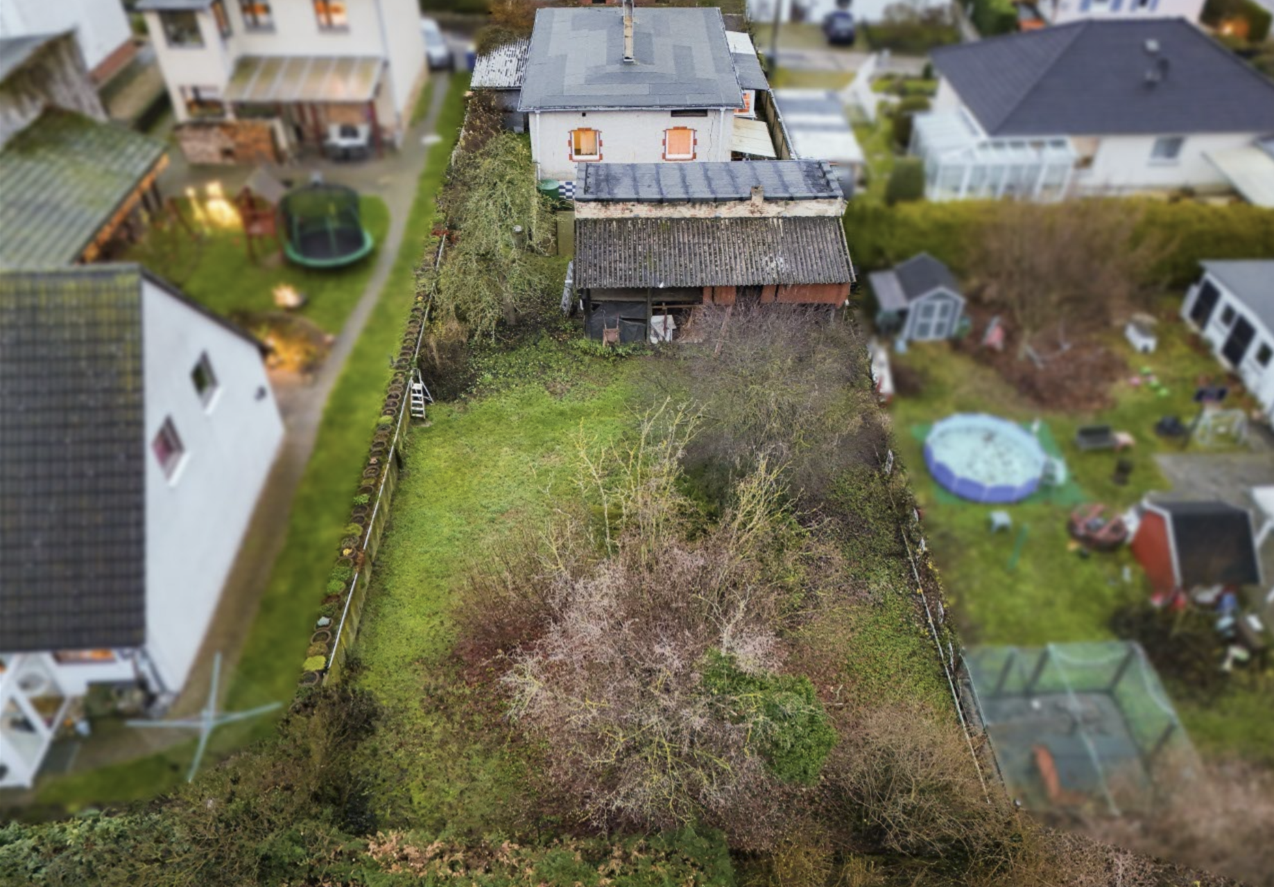 Luftaufnahme eines Gartens mit einem Wohnhaus, umgeben von Bäumen und Hecken, in einer Wohngegend.