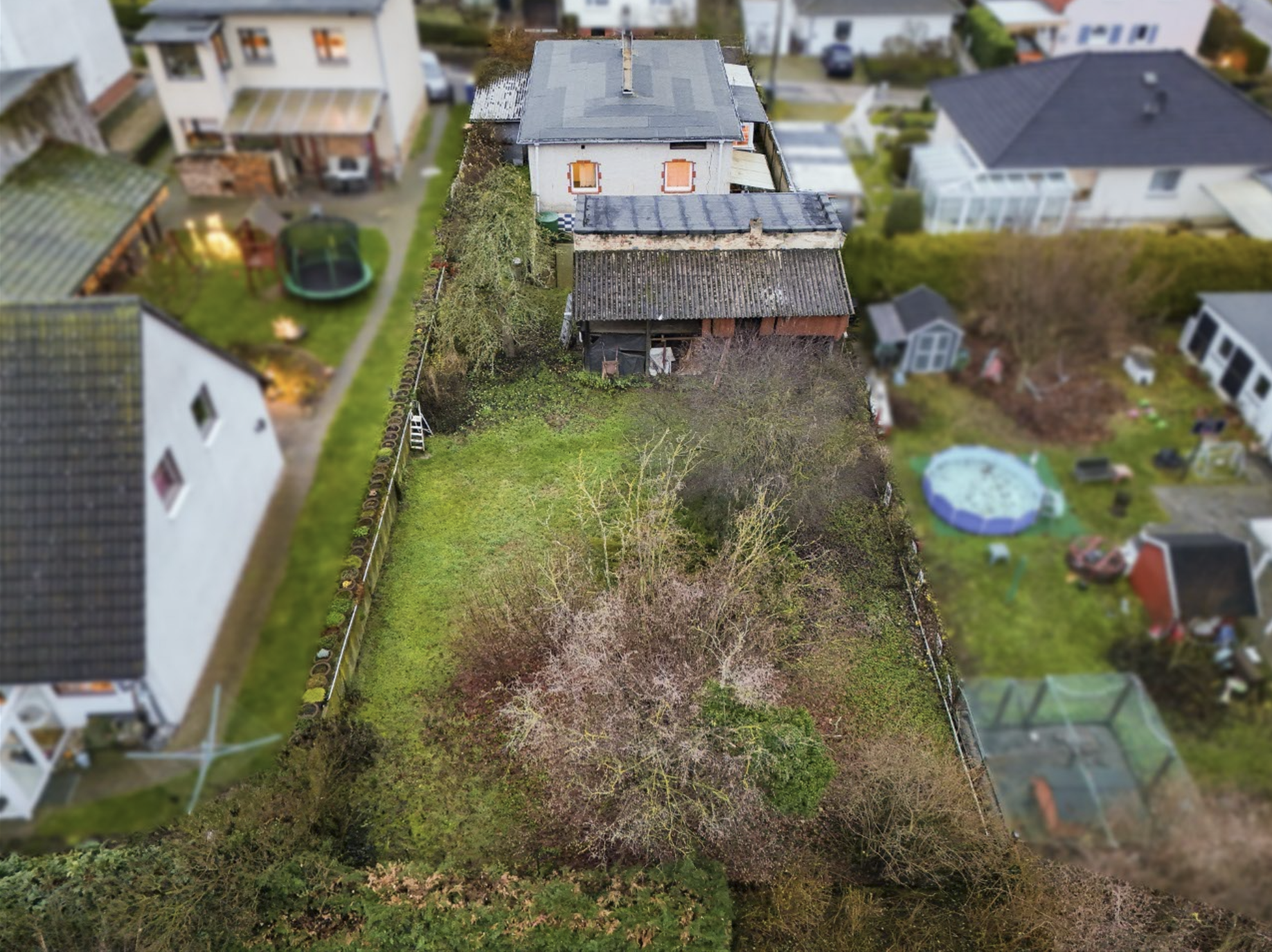 Luftaufnahme eines Gartens mit einem Wohnhaus, umgeben von Bäumen und Hecken, in einer Wohngegend.