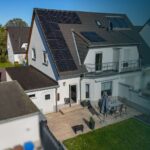 Moderne Wohnhausansicht mit Solarpanelen, Terrasse und Garten, umgeben von weiteren Einfamilienhäusern.