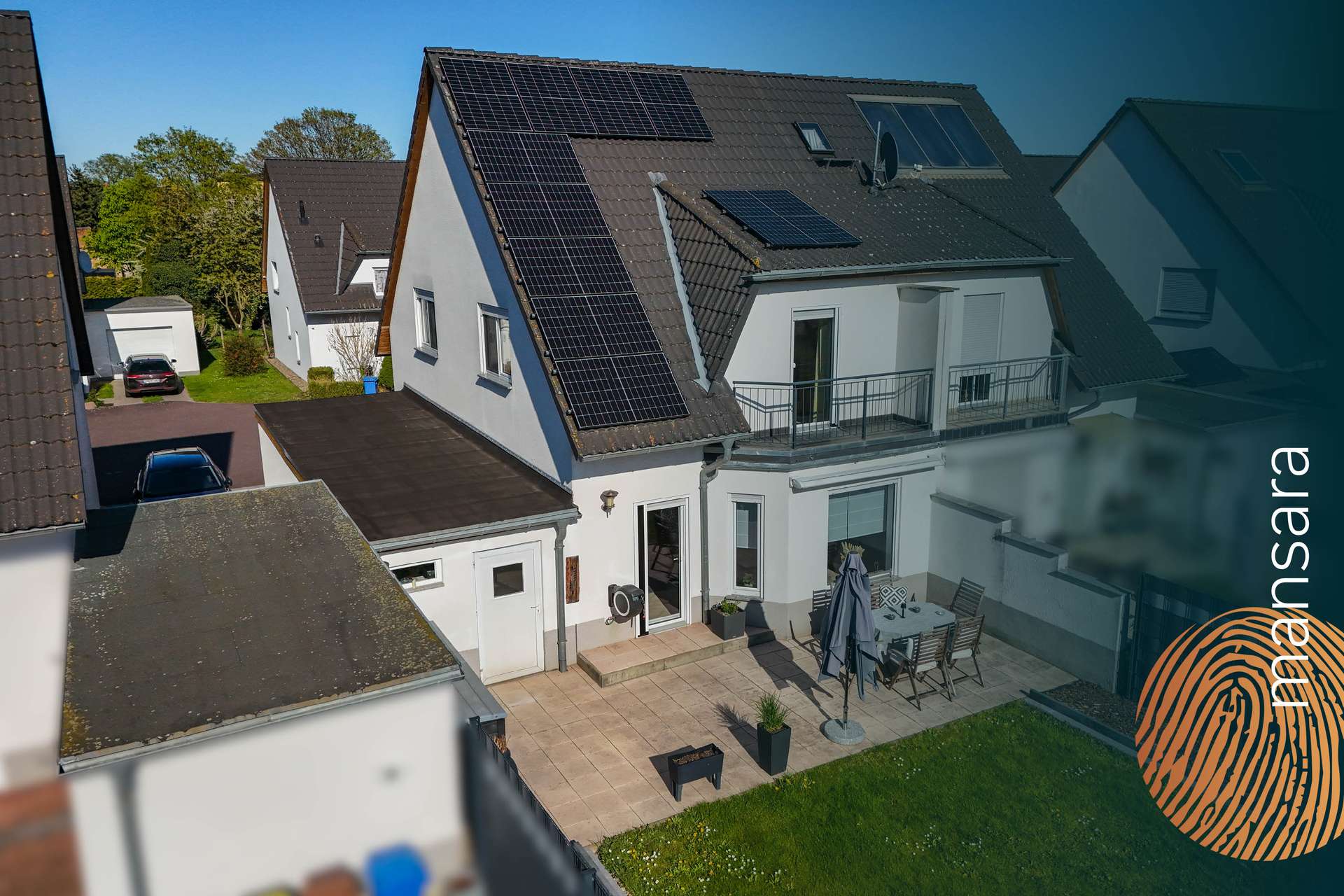 Moderne Wohnhausansicht mit Solarpanelen, Terrasse und Garten, umgeben von weiteren Einfamilienhäusern.