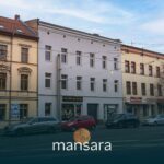 Straßenansicht eines Gebäudes mit mehreren Geschäften, darunter eine Bar, umgeben von parkenden Autos.