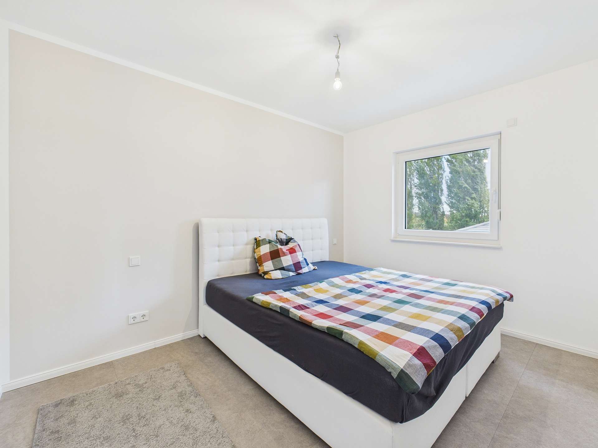 Schlafzimmer mit einem Bett, gestreift mit Kissen und einem Fenster, das Tageslicht hereinlässt.