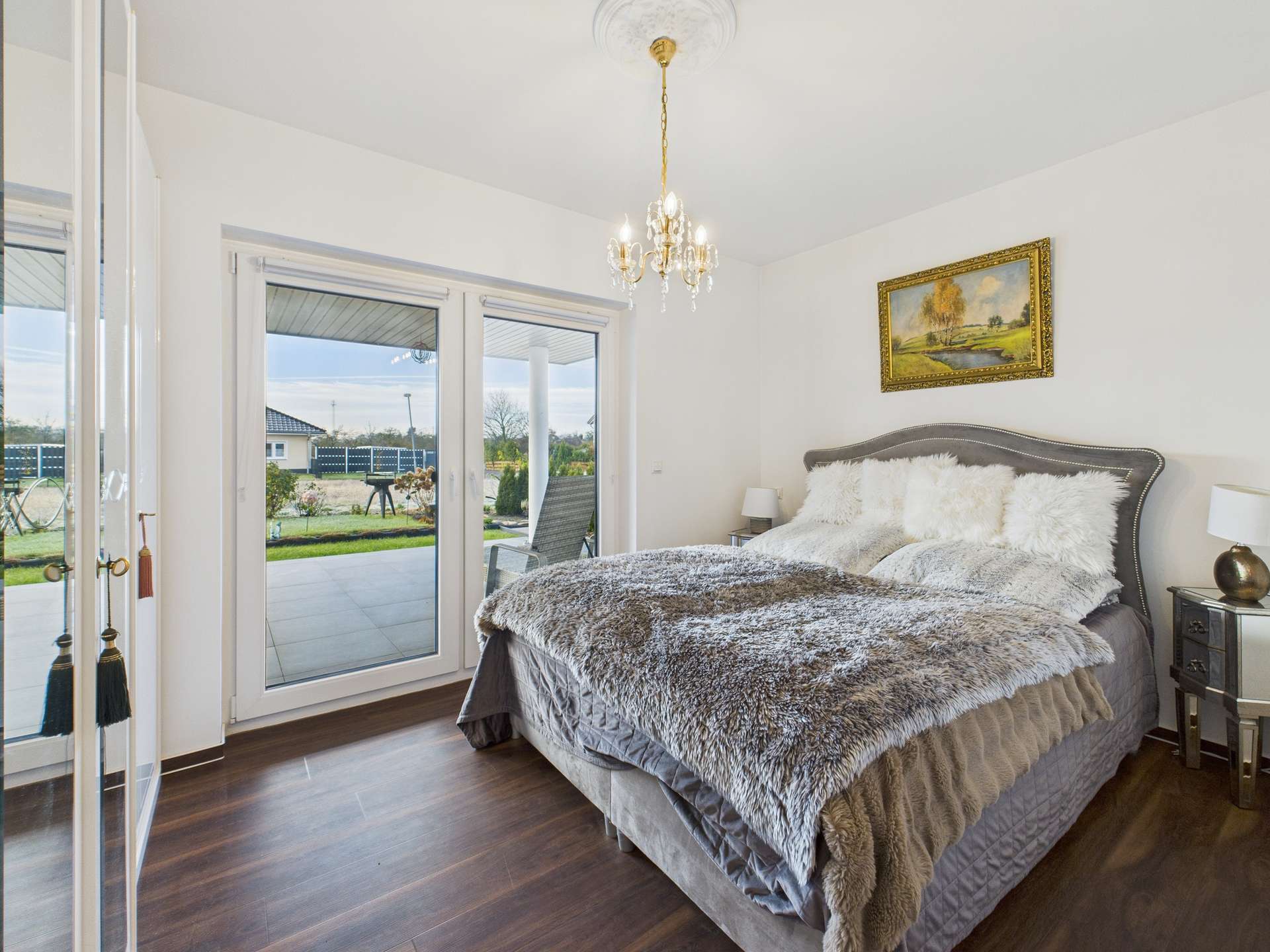 Schlafzimmer mit Doppelbett, eleganter Decke, Kunstwerk an der Wand und großen Fenstern mit Blick auf den Garten.