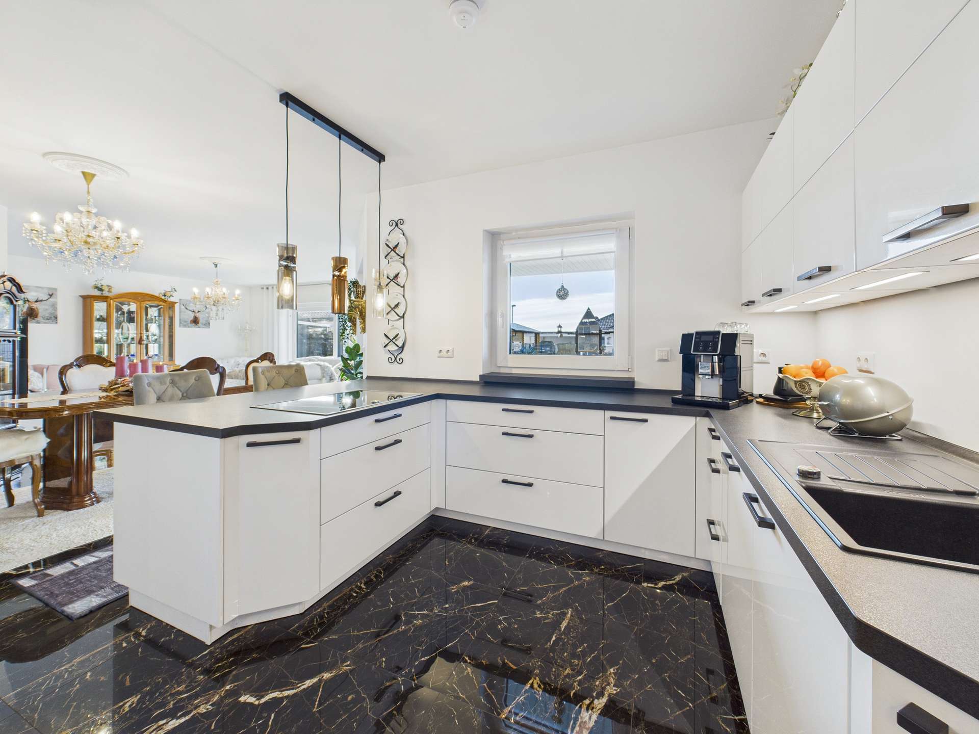 Moderne Küche mit weißen Schränken, dunklem Marmorboden und elegantem Essbereich im Hintergrund.