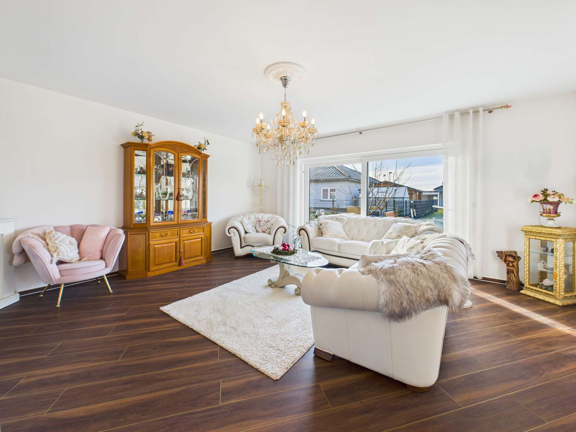 Heller Wohnraum mit weißen Sofas, einem Kronleuchter und einer Vitrine, die elegantes Interieur präsentiert.