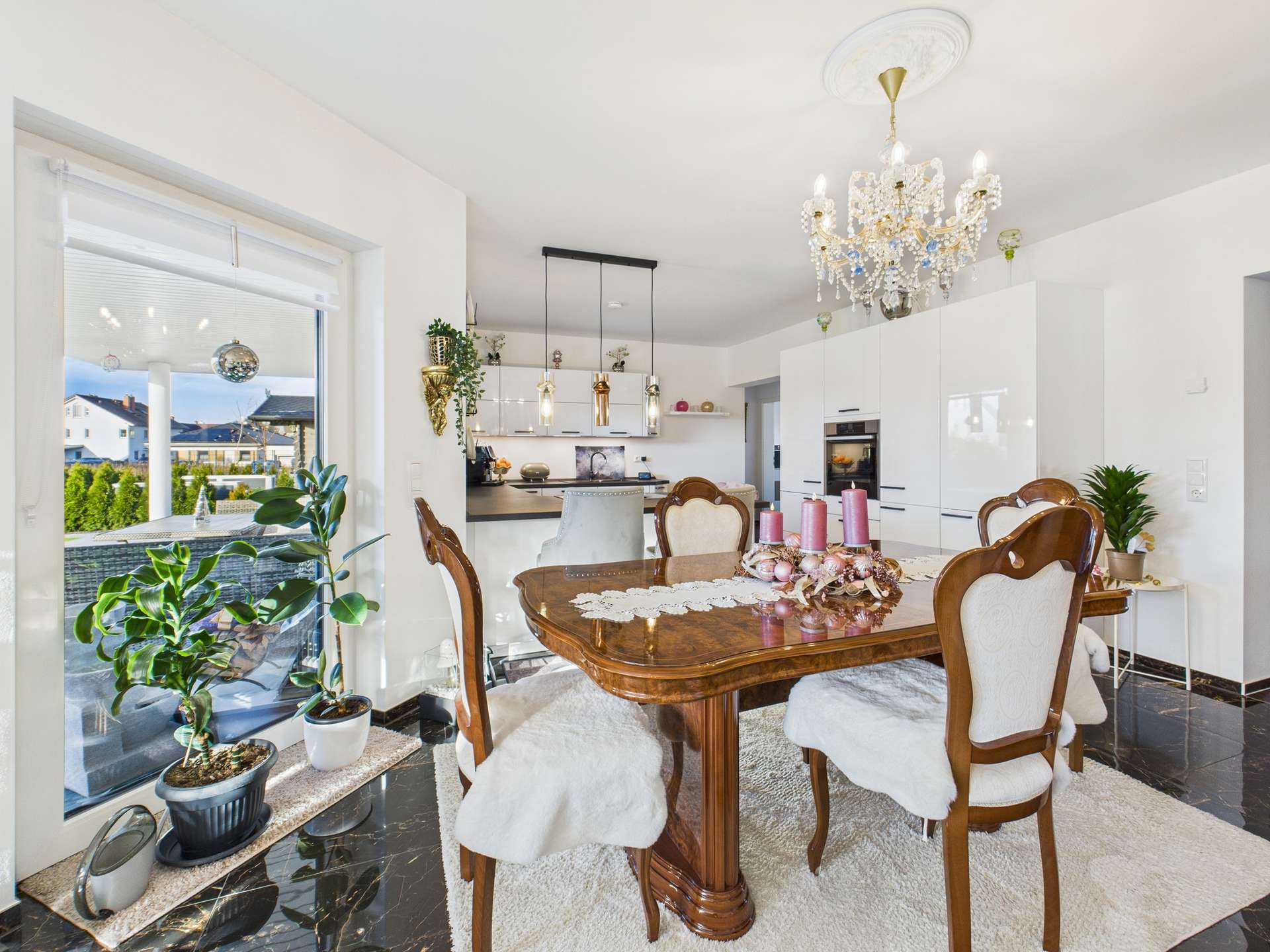 Helles Esszimmer mit Holztafel, eleganten Stühlen, moderner Küche und luxuriösem Kronleuchter.